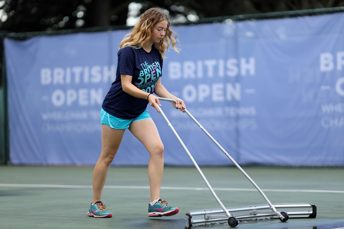 女性网球志愿者清理水从网球场雨后